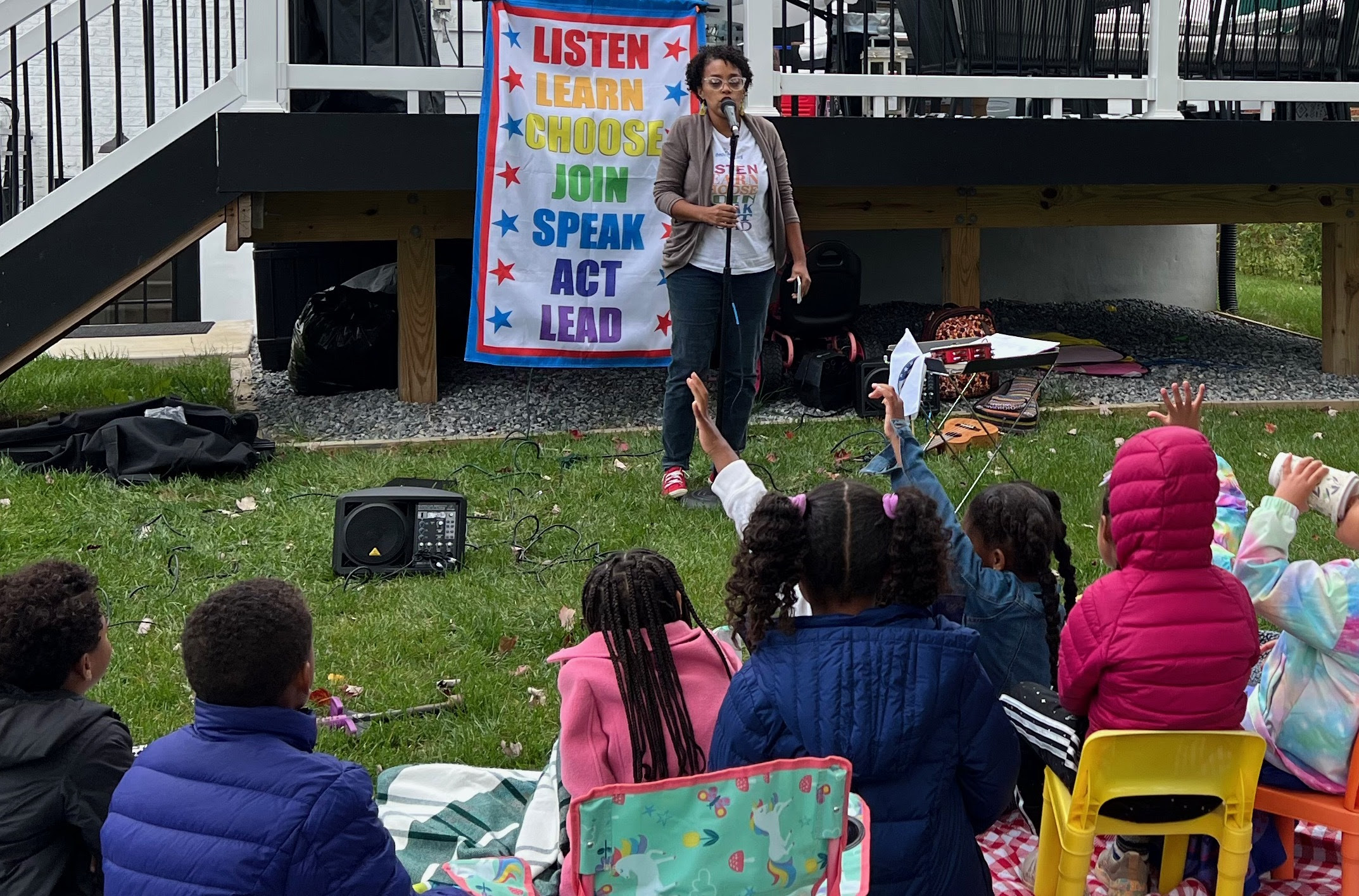 Munit Mesfin singing outside in front of a group of children, with a poster behind her that reads: "Listen Learn Choose Join Speak Act Lead"